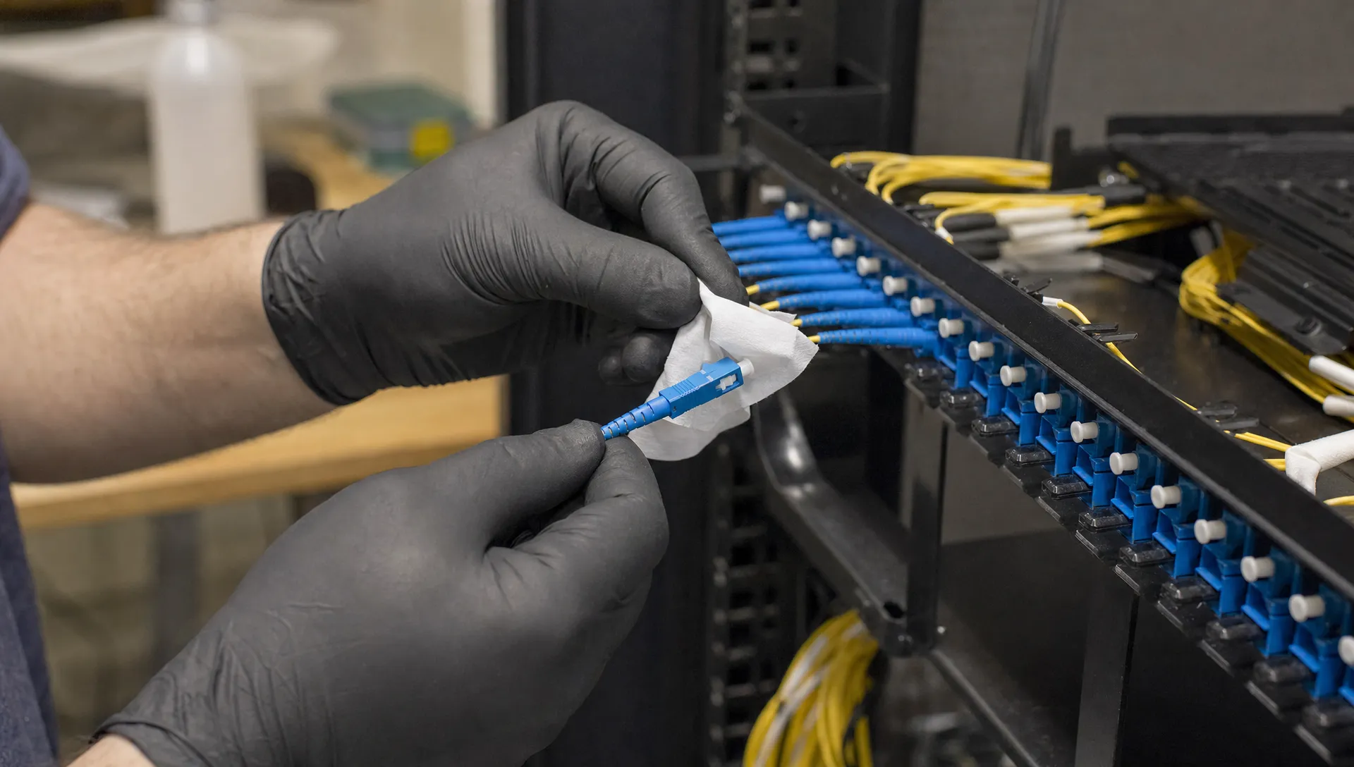 Gloved hands clean and seat a fibre connector in a patch panel for more bandbreedte.