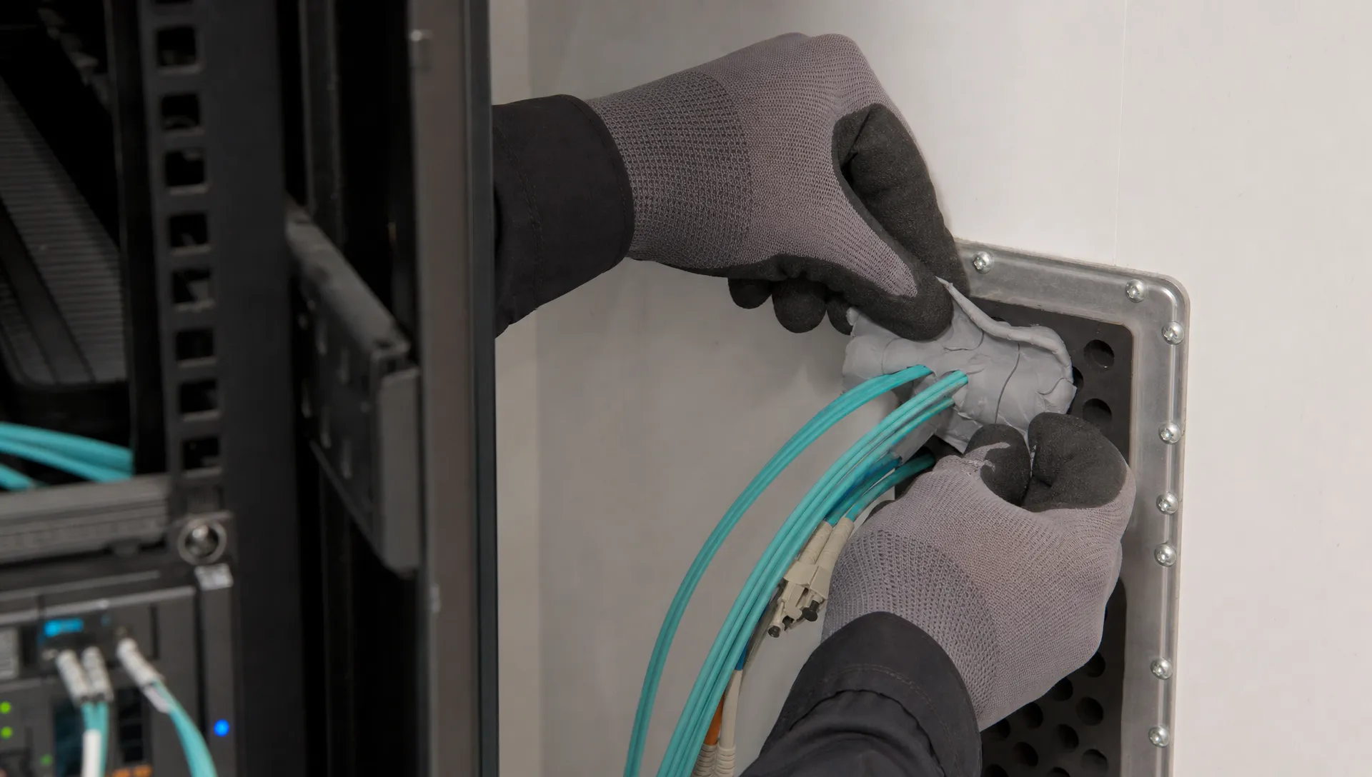 Gloved hands dichten een glasvezeldoorvoer af in een technische ruimte.